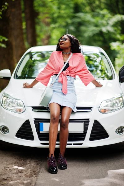 African american woman posed against white car in forest road.
