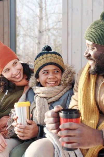 Happy cute African American boy in winterwear looking at his father during conversation while sitting between intercultural parents