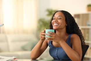 Happy black woman enjoying smelling coffee at home