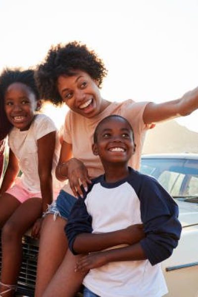 Family Posing For Selfie Next To Car Packed For Road Trip