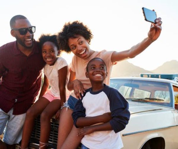 Family Posing For Selfie Next To Car Packed For Road Trip