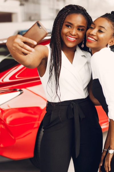 Women buying the car. Ladies in a car salon. Black girls near red car
