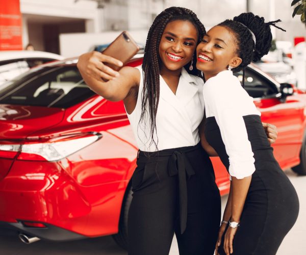 Women buying the car. Ladies in a car salon. Black girls near red car