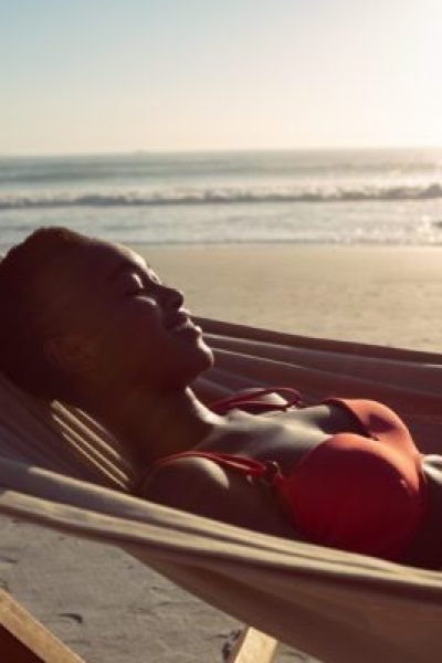 Side view of happy African-american woman using digital tablet while relaxing in a hammock on the beach